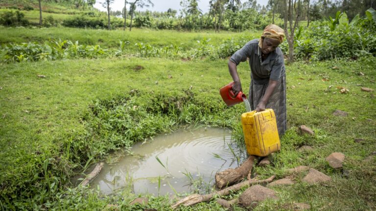 Frau schöpft Wasser aus einer verunreinigten Quelle