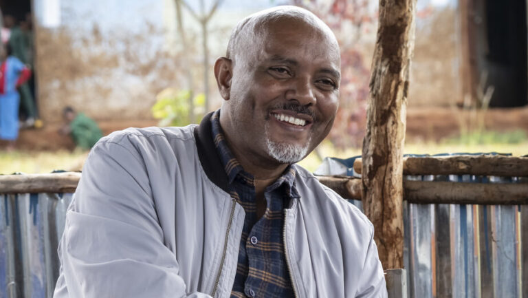 Ein lächelnder älterer Mann hält ein aufgeschlagenes Notizbuch in der Hand.