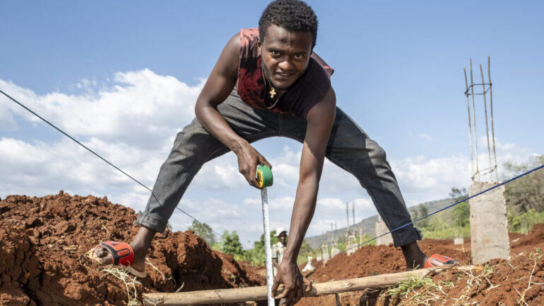 Ein junger Mann misst die Tiefe eines Grabens auf einer Baustelle.