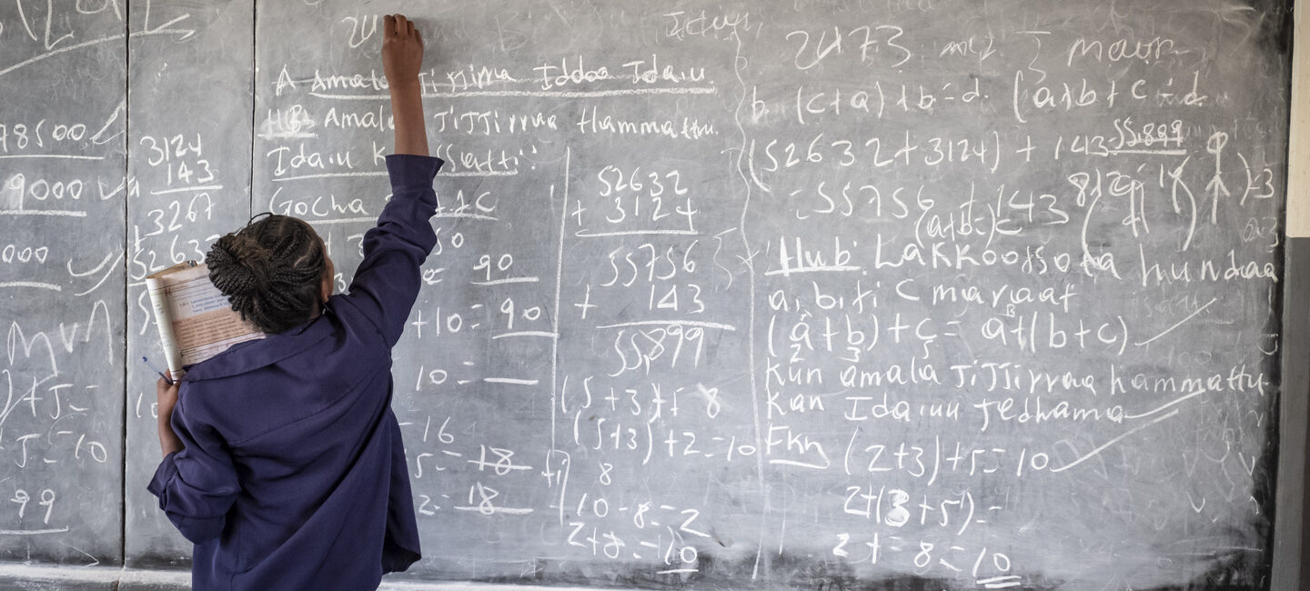 Ein Schüler schreibt einen mathematischen und fremdsprachlichen Text auf eine Kreidetafel voller Gleichungen.