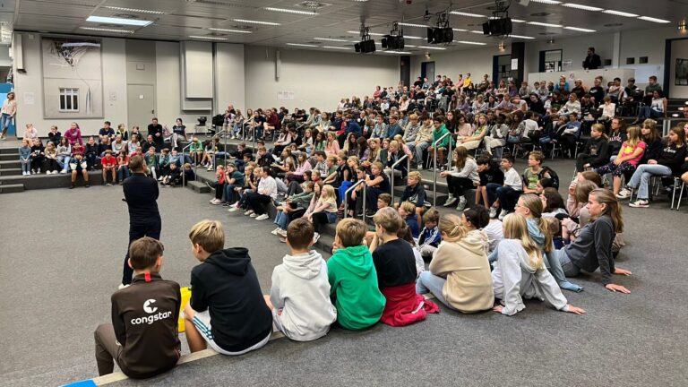 Eine Gruppe von Schülern sitzt während einer Präsentation in einer Schulaula und hört zu.