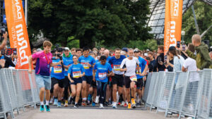 Läufer an der Startlinie eines Rennens, mit jubelnden Zuschauern und Veranstaltungsbannern im Hintergrund.