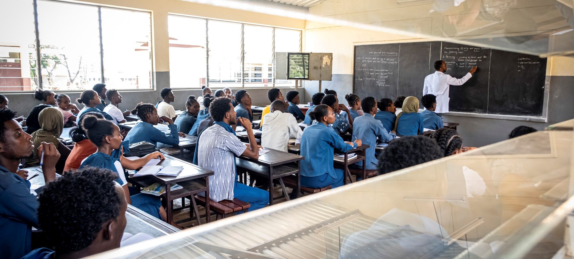 Der Lehrer schreibt an die Tafel, während die Schüler in Uniform im Klassenzimmer zuhören.