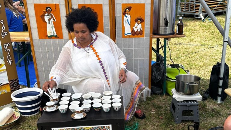 Eine Frau in traditioneller Kleidung arrangiert draußen Tassen für eine äthiopische Kaffeezeremonie.