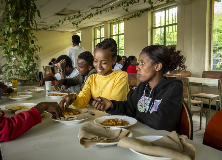 Junge Studenten unterhalten sich beim Mittagessen in einer mit Pflanzen gefüllten Kantine.