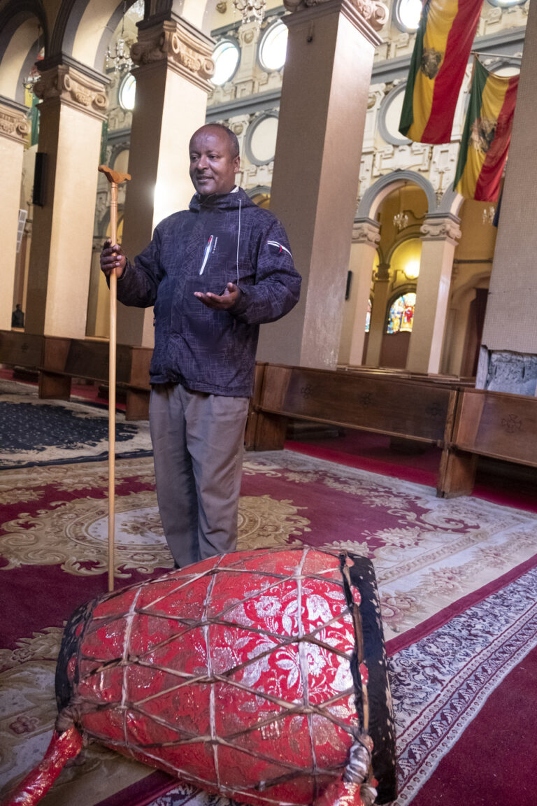 Mann mit Kabaro steht in der Nähe von Die Wunderpflanze Zierbanane in einem geschmückten Saal, drinnen.
