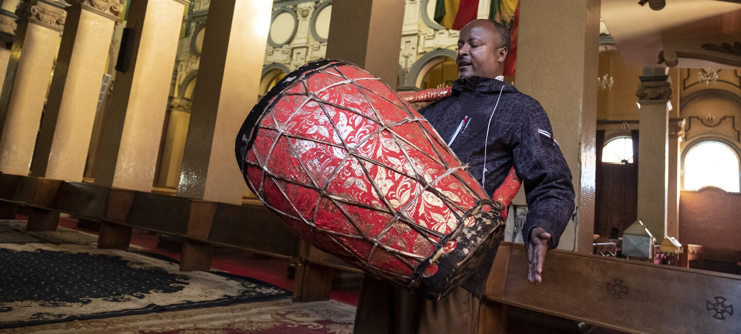 Ein Mann spielt eine große rote Trommel in einer verzierten Kirche.
