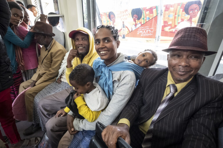 Lächelnde Menschen sitzen auf einer Bank. In der Mitte sitzt eine Frau mit zwei Kindern.