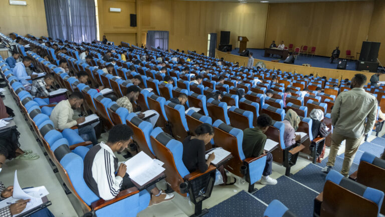 Die Studenten sitzen in Reihen von blauen Stühlen und schreiben gemeinsam eine Prüfung in einem geräumigen Hörsaal.