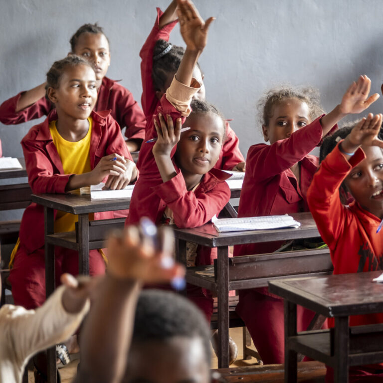 Lächelnde Kinder in roten Uniformen heben eifrig ihre Hände in einem hellen Klassenzimmer.