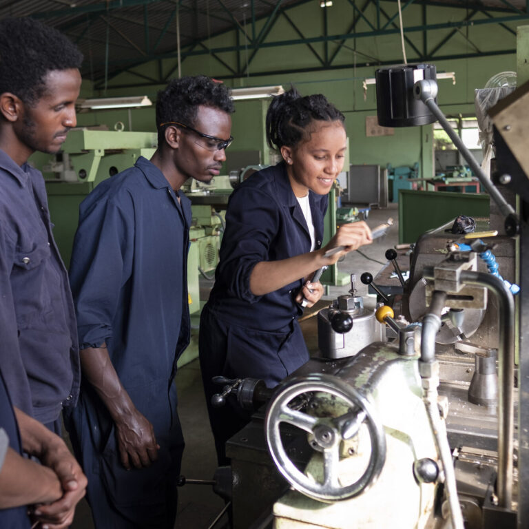 Drei Arbeiter in Schutzanzügen setzen in einer Industriehalle Maschinen ein und veranschaulichen damit ihre Teamarbeit.