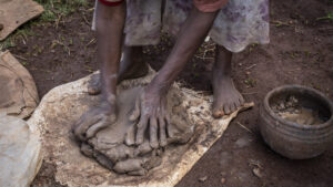 Eine Frau knetet nassen Ton auf einer Matte im Freien.
