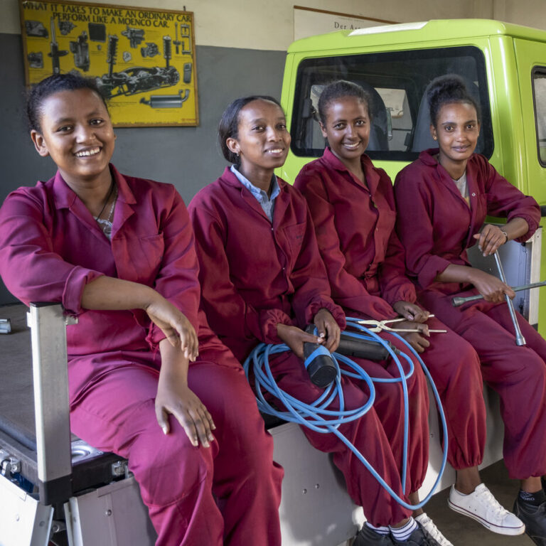 Vier Frauen in kastanienbraunen Overalls lächeln gemeinsam in einer Autowerkstatt und unterstützen Spenden von NRO.