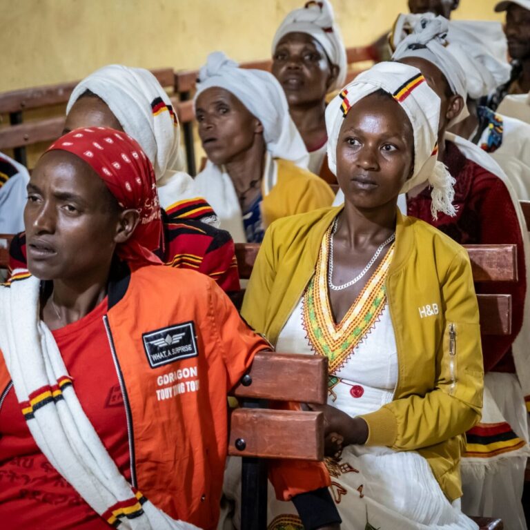 Frauen in traditioneller Kleidung und mit Kopftüchern sitzen auf Bänken und hören bei einer Veranstaltung einer NRO aufmerksam zu.