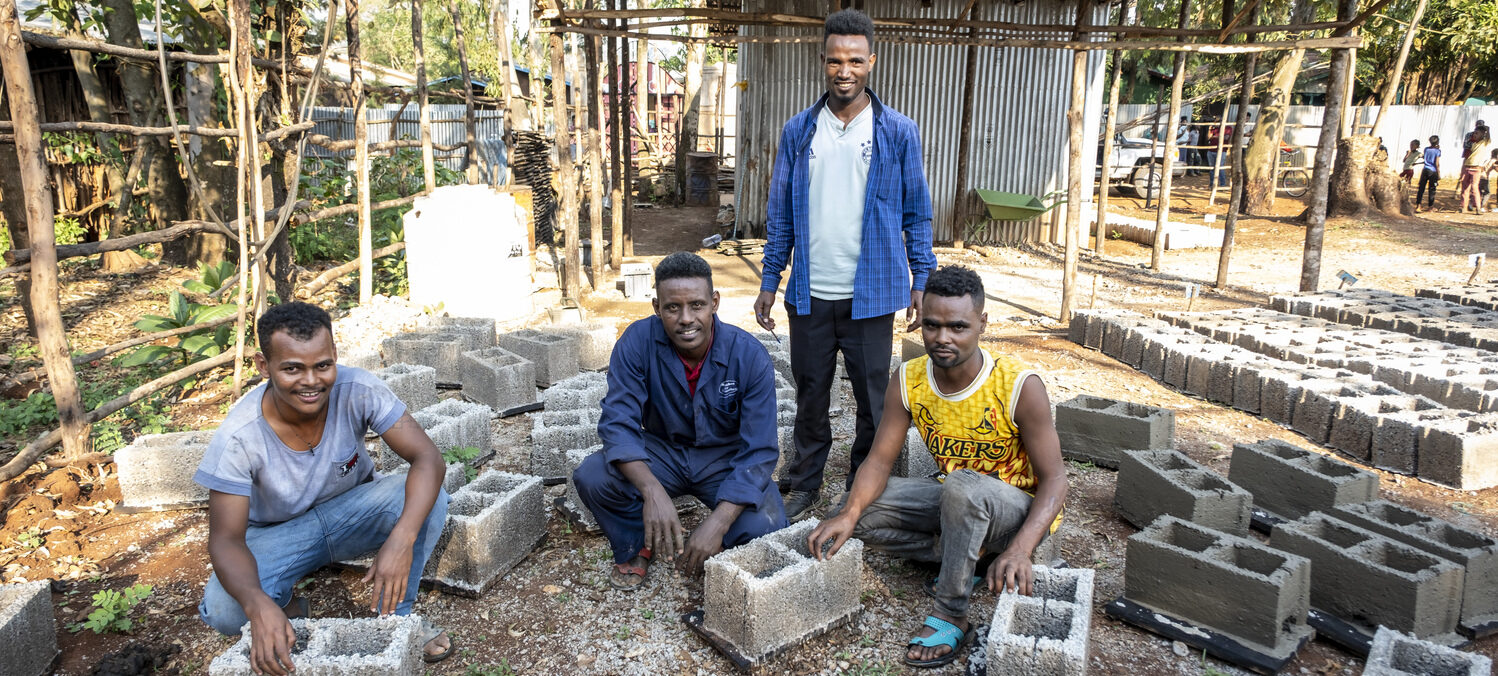 Vier Männer lächeln, während sie auf einer Baustelle für ein NRO-Projekt Betonblöcke herstellen.