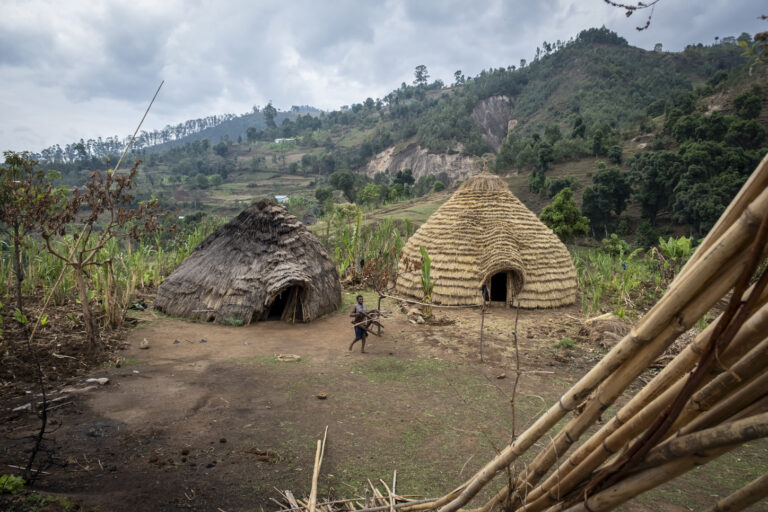 Zwei strohgedeckte Hütten inmitten von Hügeln und Feldern.