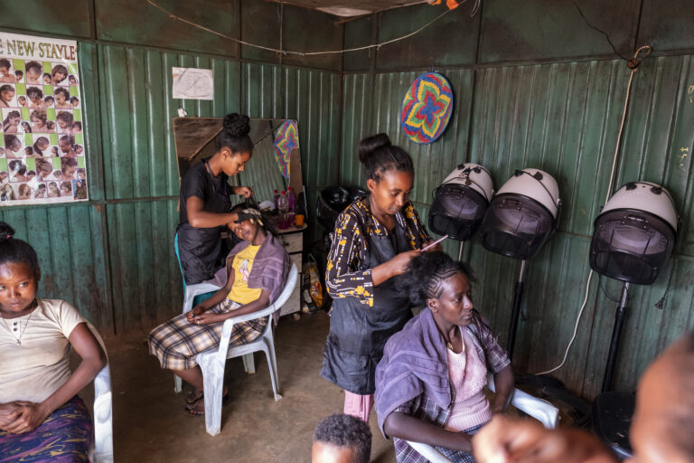 Frauen werden in einem lebhaften Salon mit Haartrocknern und Frisurenpostern an den Wänden frisiert.