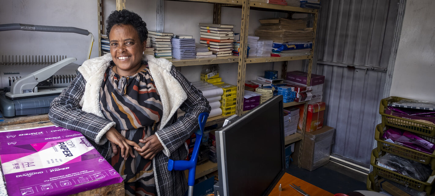 Eine lächelnde Frau in ihrem Copyshop, umgeben von Akten.