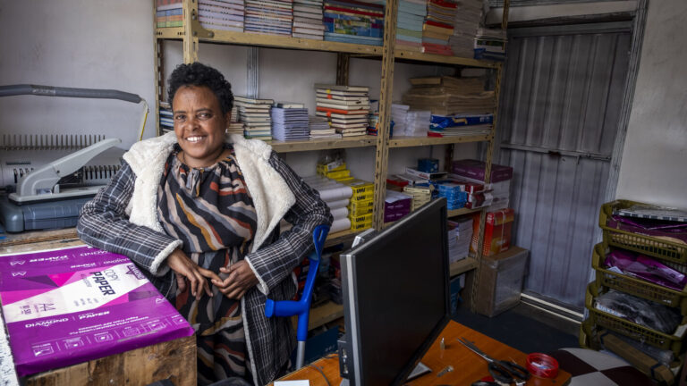 Eine lächelnde Frau in ihrem Copyshop, umgeben von Akten.