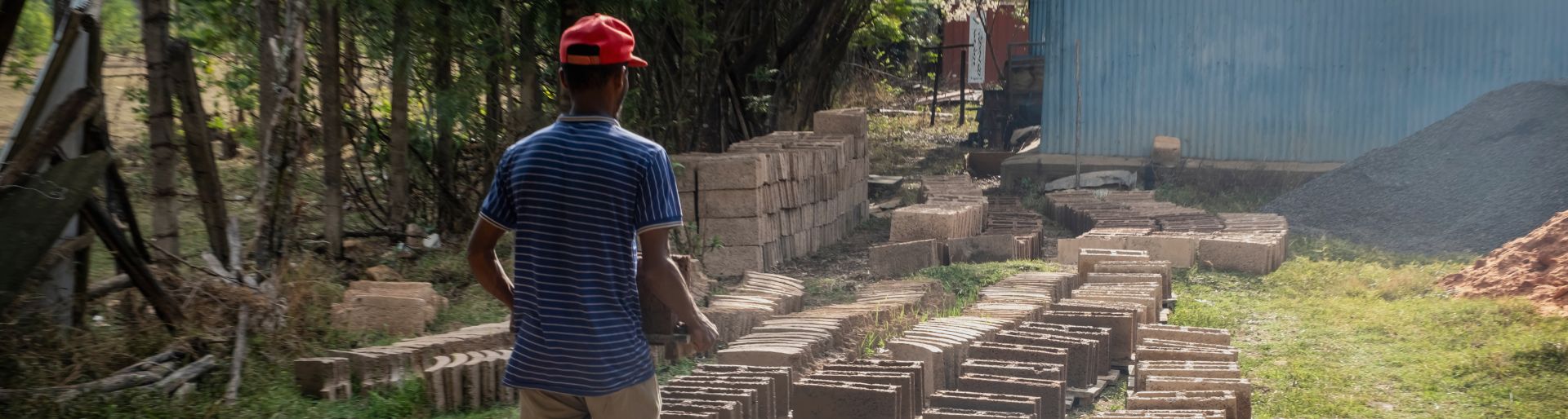 Ein Mann mit roter Mütze steht vor gestapelten Betonblöcken und Ziegeln auf der Baustelle eines Spendenprojekts.