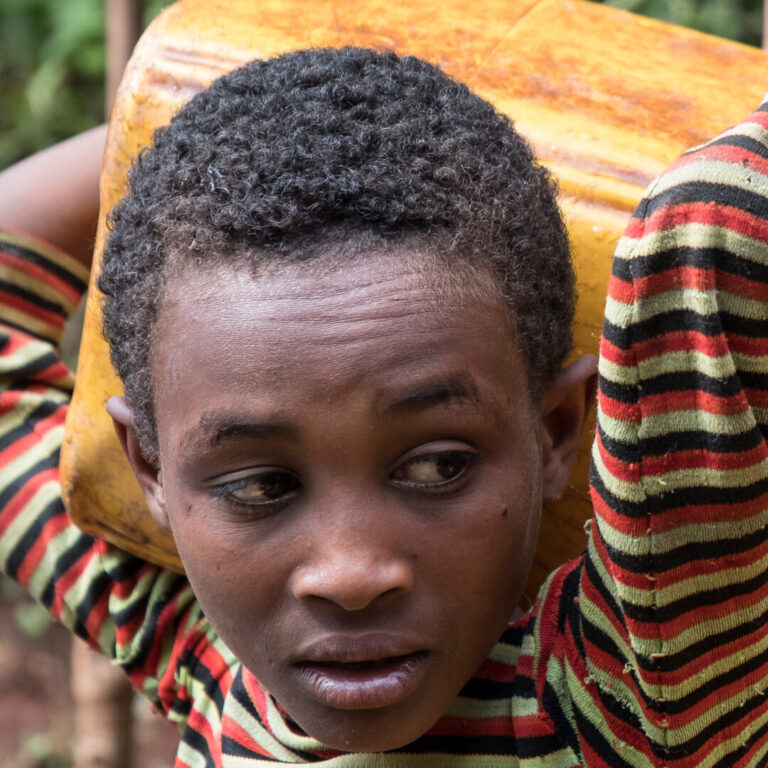 Kind mit kurzem lockigem Haar trägt einen gelben Behälter auf der Schulter und schaut zur Seite.