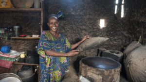 Eine lächelnde Frau bereitet in ihrer Küche mit einem grünen Ofen aus Ton Essen zu.