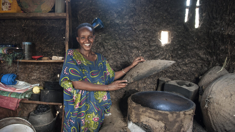 Eine lächelnde Frau bereitet in ihrer Küche mit einem grünen Ofen aus Ton Essen zu.