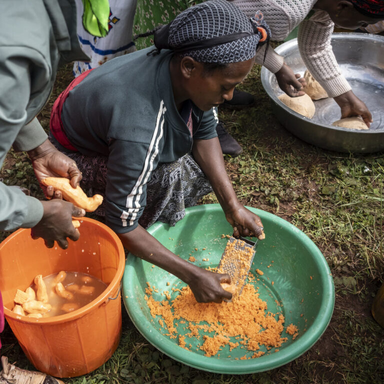 Eine Frau kniet am Boden und zerkleinert Süßkartoffeln.