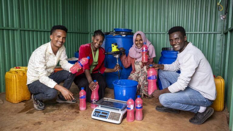 Vier junge Menschen präsentieren ihre selbst produzierte Seife, die sie in Flaschen verkaufen.