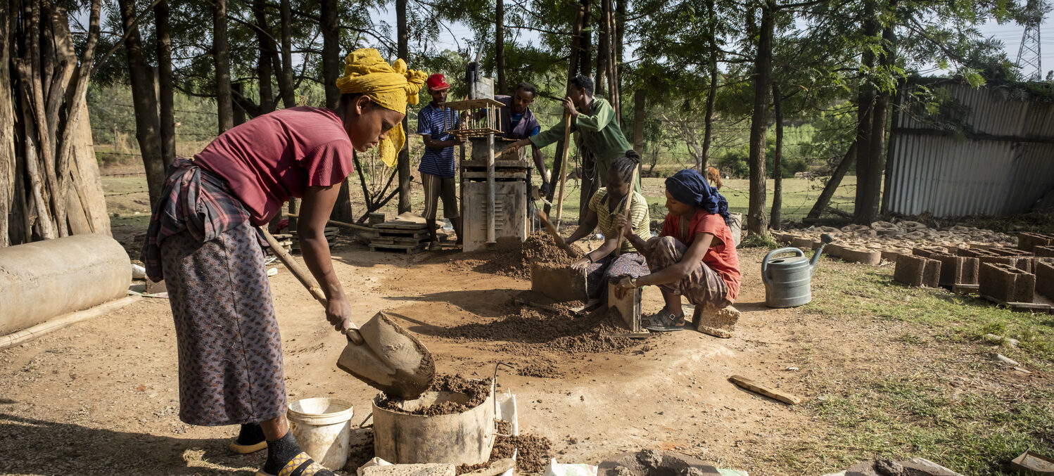 Junge Menschen produzieren draußen Ziegelsteine und holzsparende Öfen.
