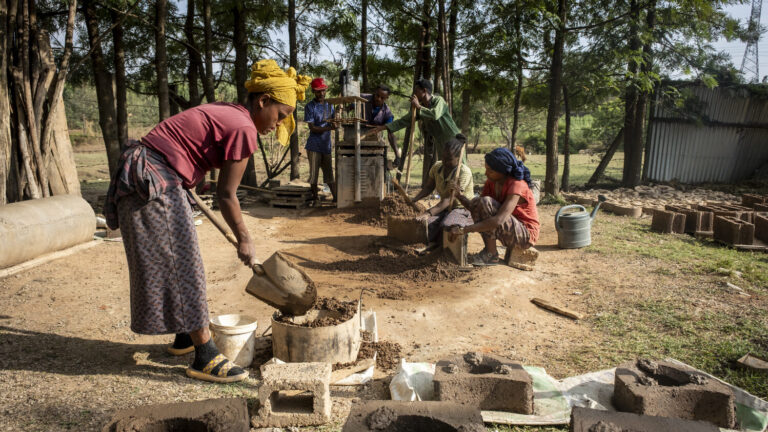 Junge Menschen produzieren draußen Ziegelsteine und holzsparende Öfen.