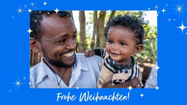 Ein lächelnder Vater aus Äthiopien hält sein kleines Kind. Es grinst begeistert.