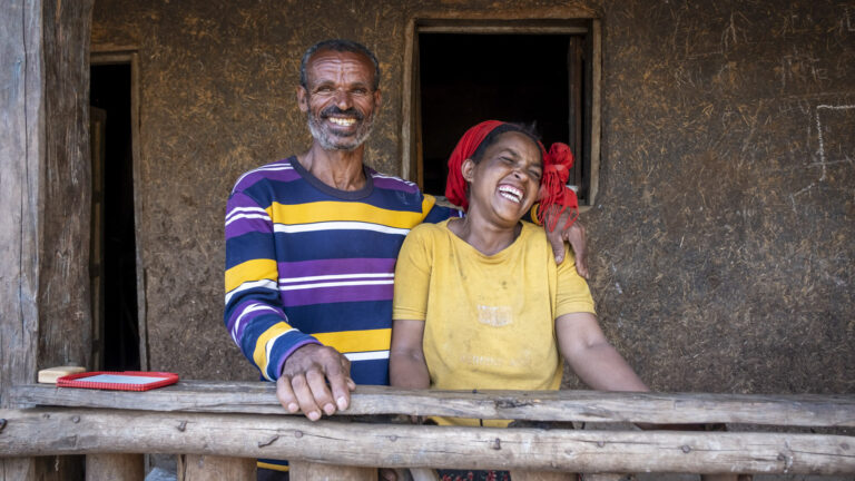 Ein lächelnder Mann und eine lächelnde Frau stehen Seite an Seite auf einer Veranda.