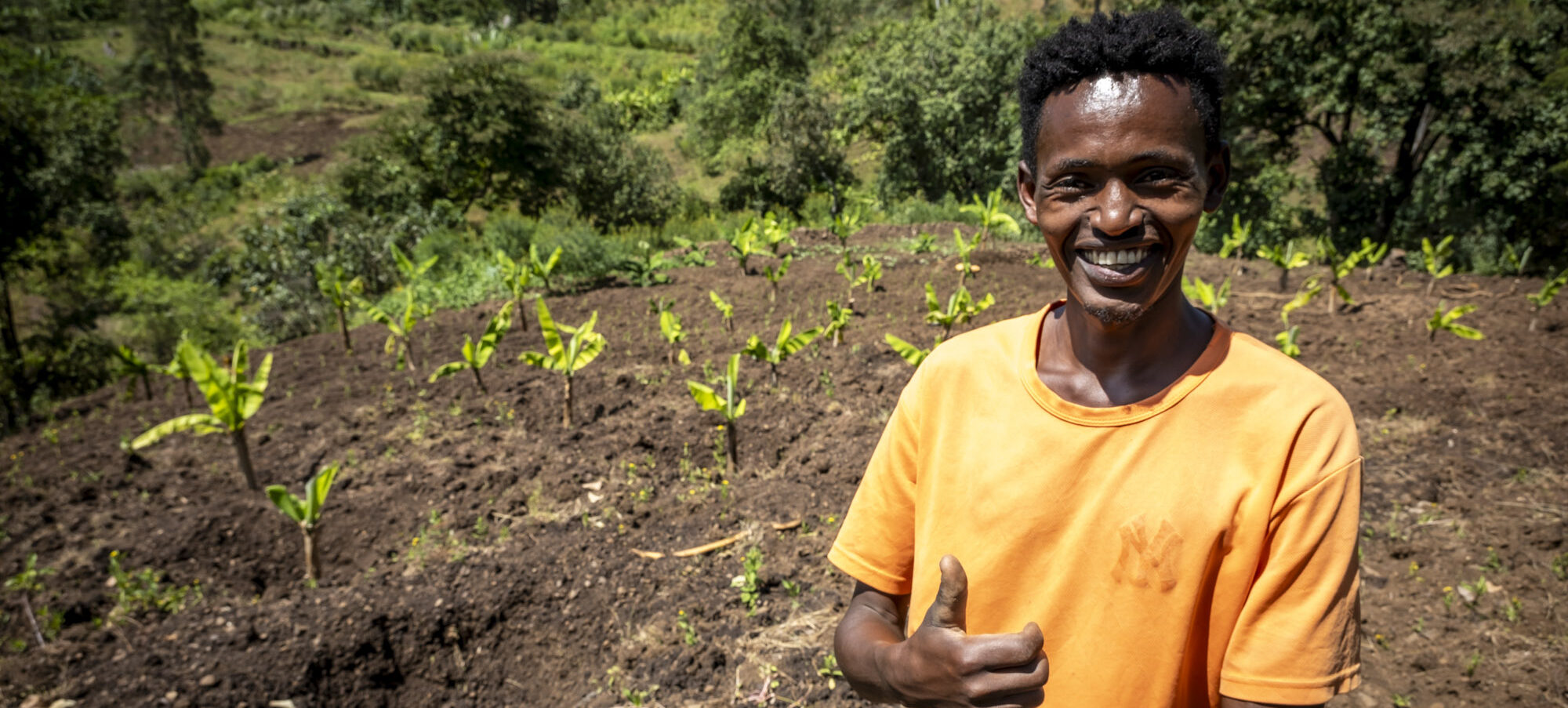 Ein junger Mann steht lachend auf dem Feld, das er bewirtschaftet.