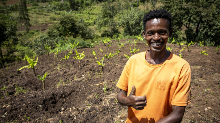 Ein junger Mann steht lachend auf dem Feld, das er bewirtschaftet.