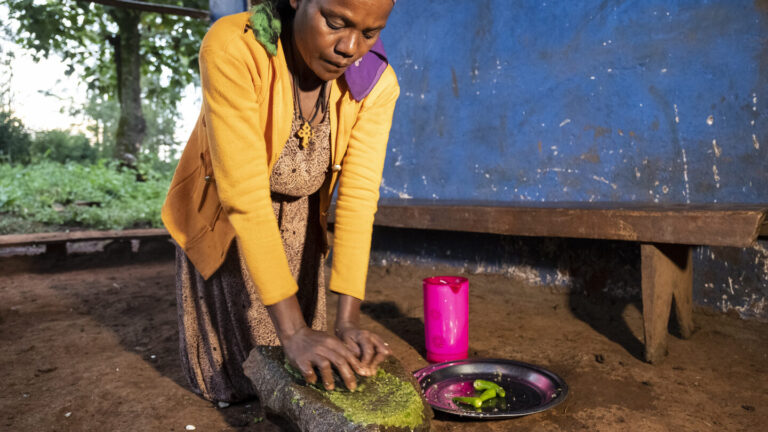 Eine Frau zerkleinert in einem Haus grüne Chilipaste Qochqocha.
