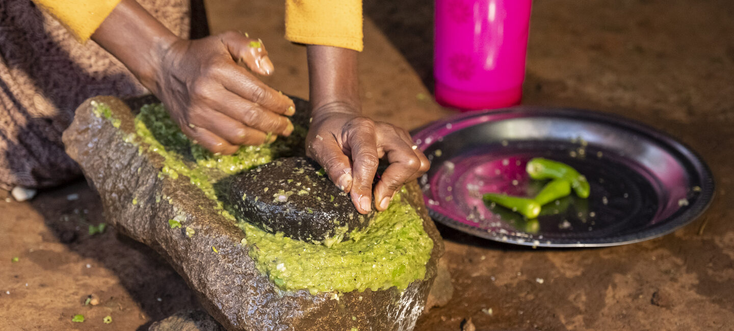 Hände, die grüne Chilis auf einem Stein zerkleinern.