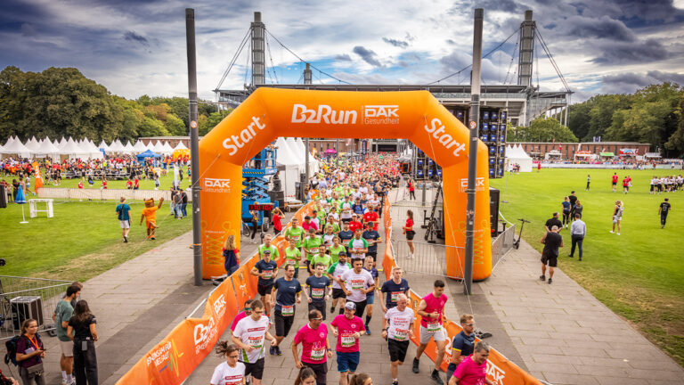 Teilnehmer eines Firmenlaufs joggen durch einen Torbogen von B2Run.
