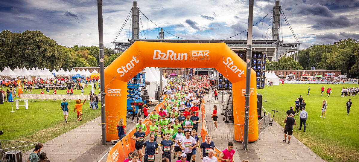 Teilnehmer eines Firmenlaufs joggen durch einen Torbogen von B2Run.