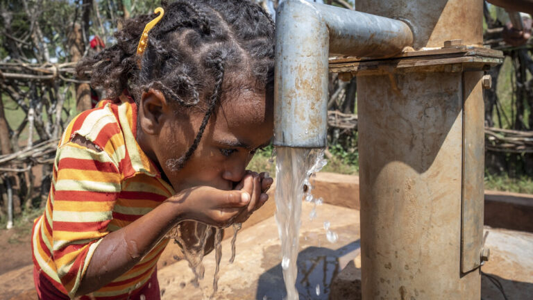 Ein Mädchen, das am Brunnen Wasser in ihre Hände fließen lässt und daraus trinkt.