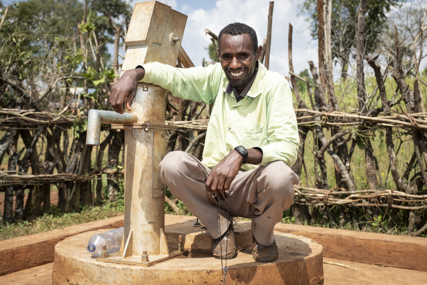 Dhabasa Fite, der Brunnenwächter kniet neben dem Brunnen mit einem Arm locker über die Handpumpe gelegt.