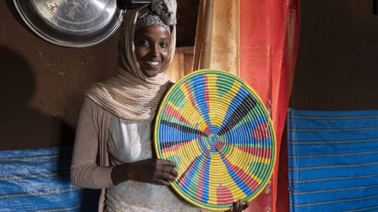 Derartu hält einen bunten geflechteten Korbteller in den Händen.