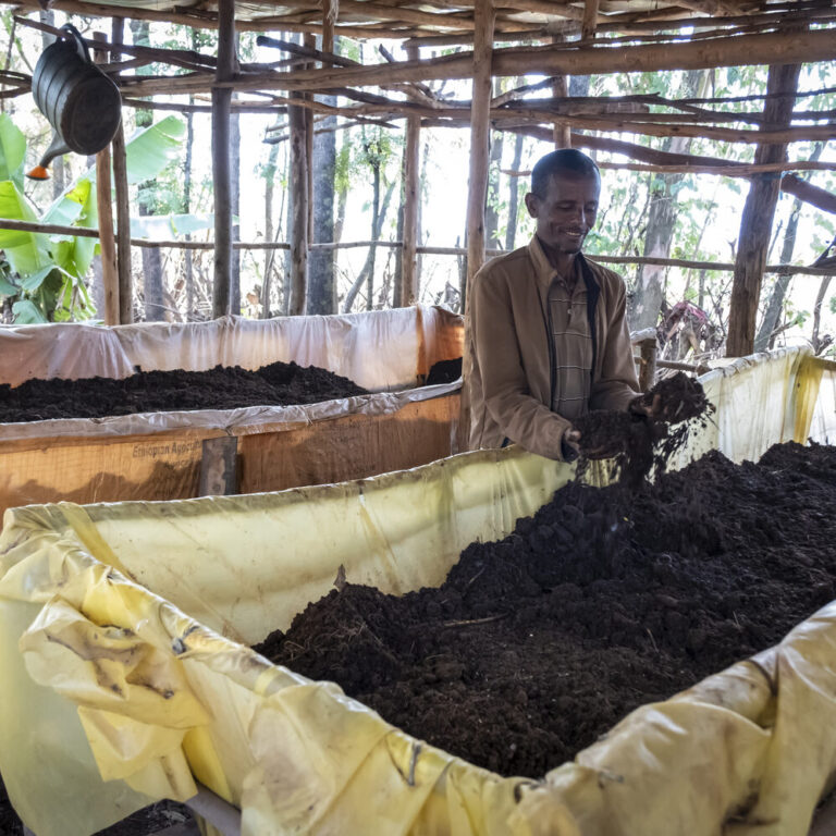 Ein Landwirt steht vor seiner großen Kompostkiste und freut sich über neue Komposterde.