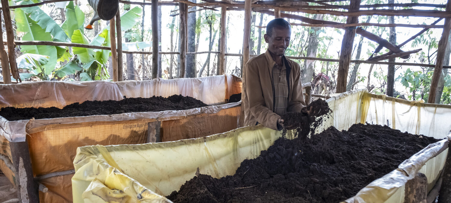 Ein Landwirt steht vor seiner großen Kompostkiste und freut sich über neue Komposterde.