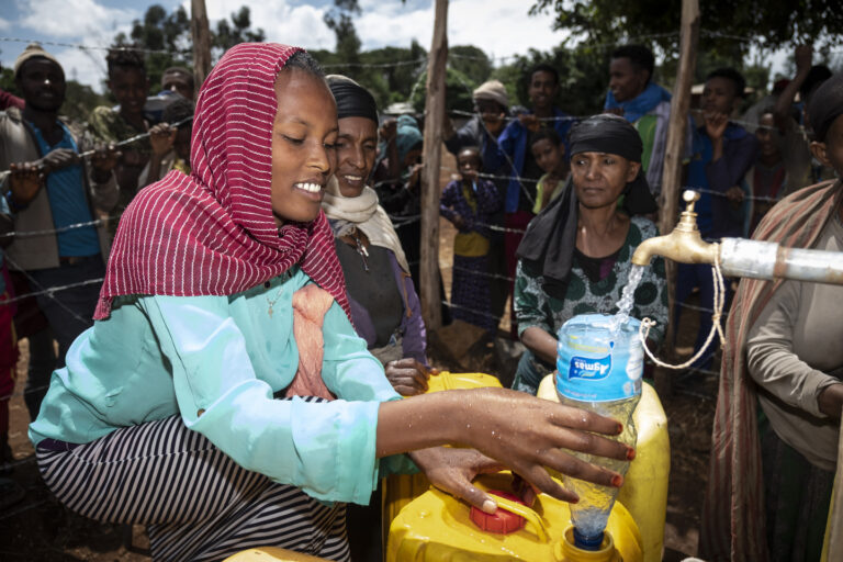 Eine junge Frau lässt Wasser durch einen Trichter in ihren Wassercontainer fließen.