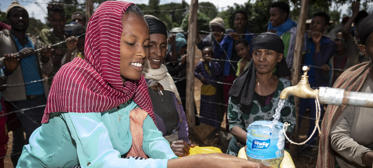 Eine Frau die Wasser aus einem Wasserhahn in ihren Kanister gießt.