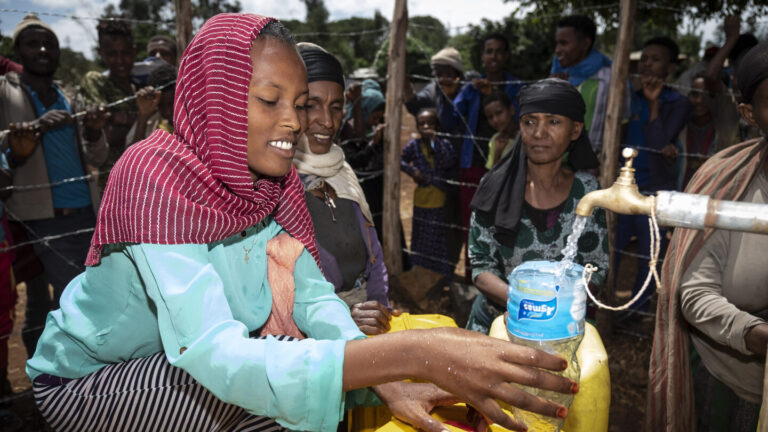 Eine Frau die Wasser aus einem Wasserhahn in ihren Kanister gießt.