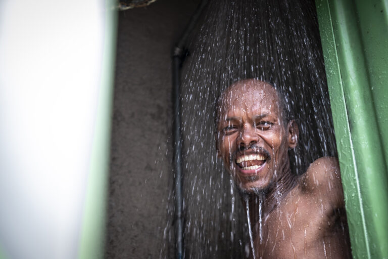 Ein Mann der lachend in die Kamera schaut und Wasser über sein Kopf fließt.