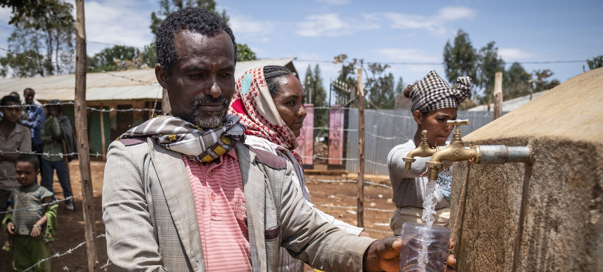 Ein Mann der an einem Brunnen Wasser in seinen Kanister füllt.