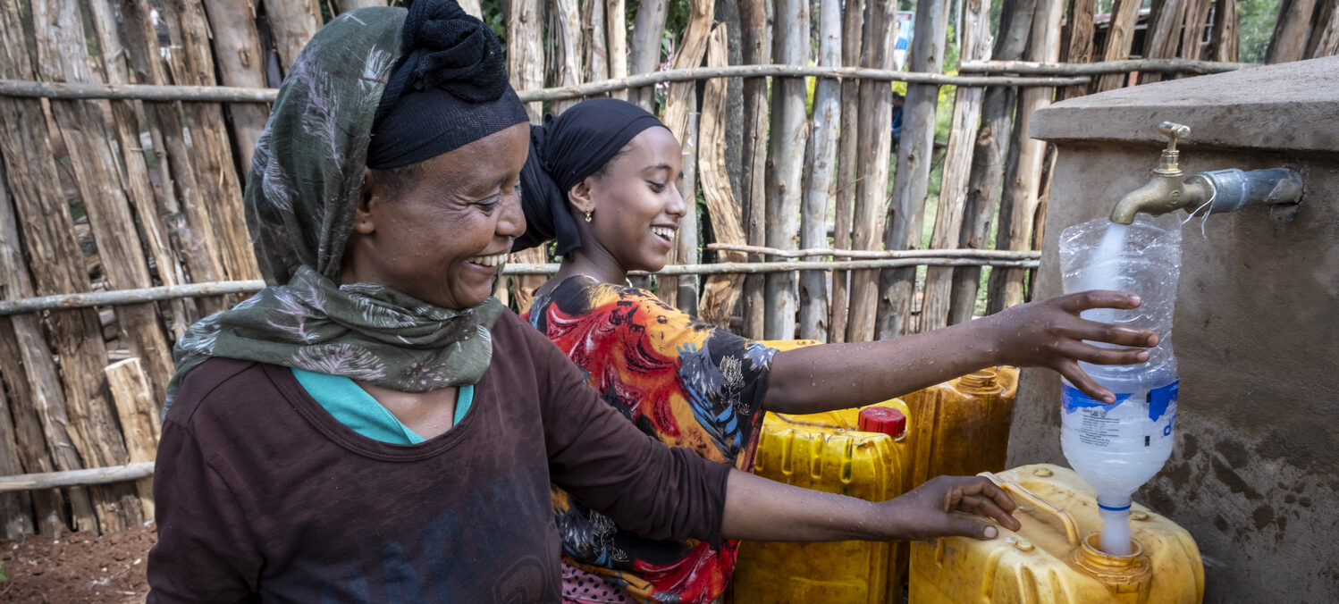 Zwei Frauen füllen frisches Trinkwasser in gelbe Kanister ab.